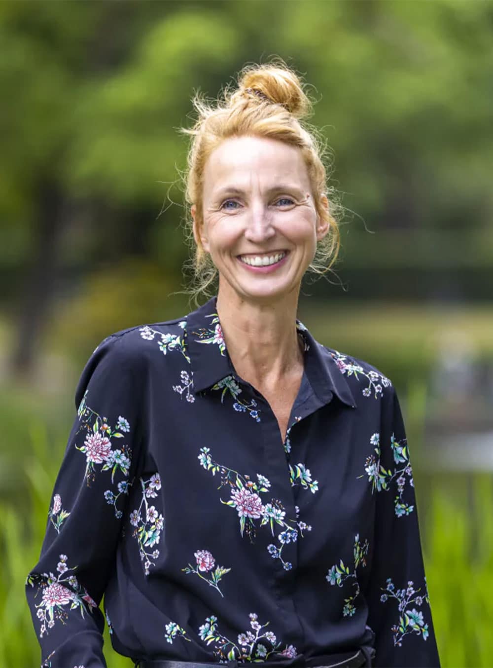 Porträt einer Frau mit blauer Bluse und Blumenmuster Frau mit blonden Haaren, die zu einem Dutt gebunden sind, trägt eine blaue Bluse mit Blumenmuster.