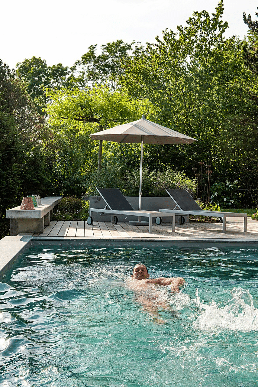 Schwimmer im Pool mit Liegen und Sonnenschirm Ein Mann schwimmt im Pool, während Liegen und ein Sonnenschirm im Hintergrund sichtbar sind.