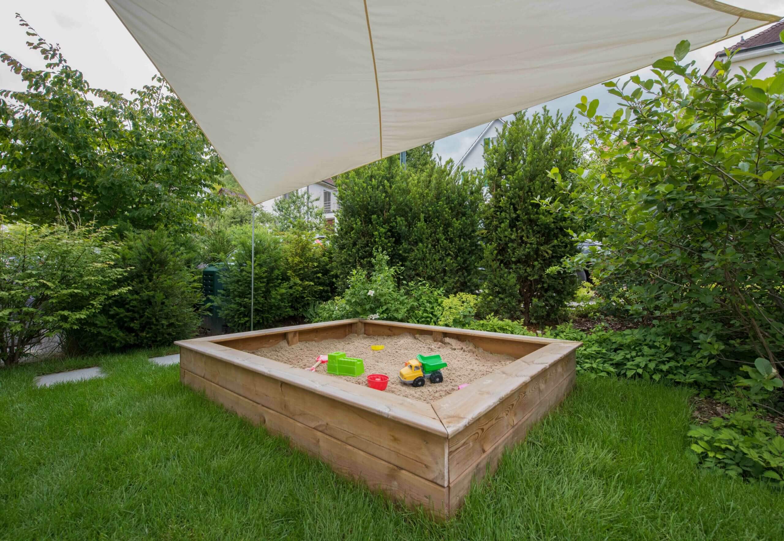 Sandkasten im Garten mit Spielzeug Holz-Sandkasten im Garten mit Spielzeugtraktor und Schaufel unter einem Sonnenschutz.