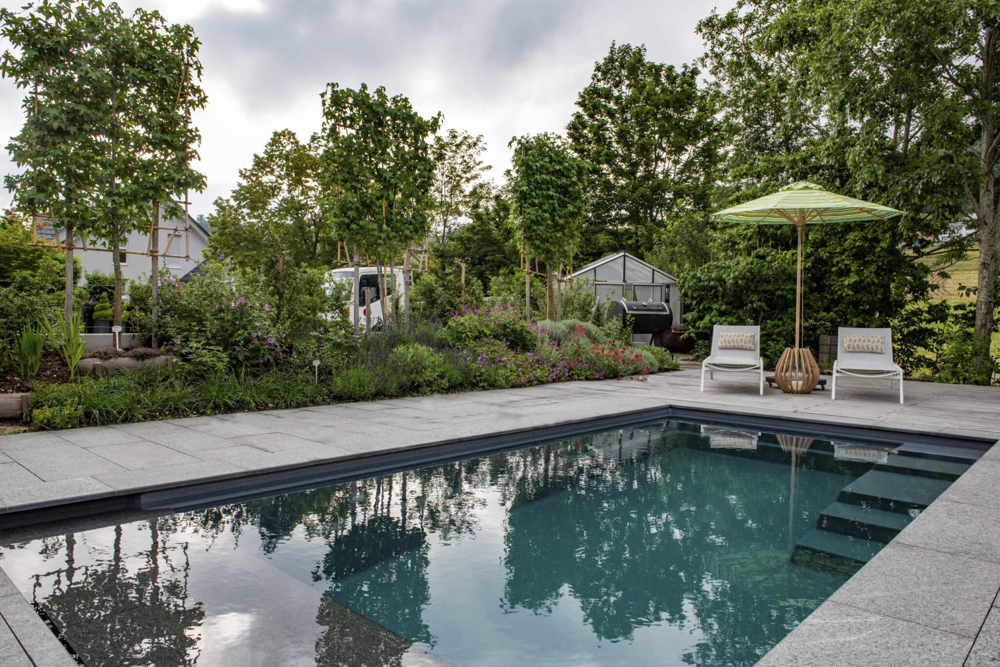 Gepflegter Garten mit rechteckigem Pool, üppigen Pflanzen, Liegestühlen und Sonnenschirm bei Forster Gartenbau AG