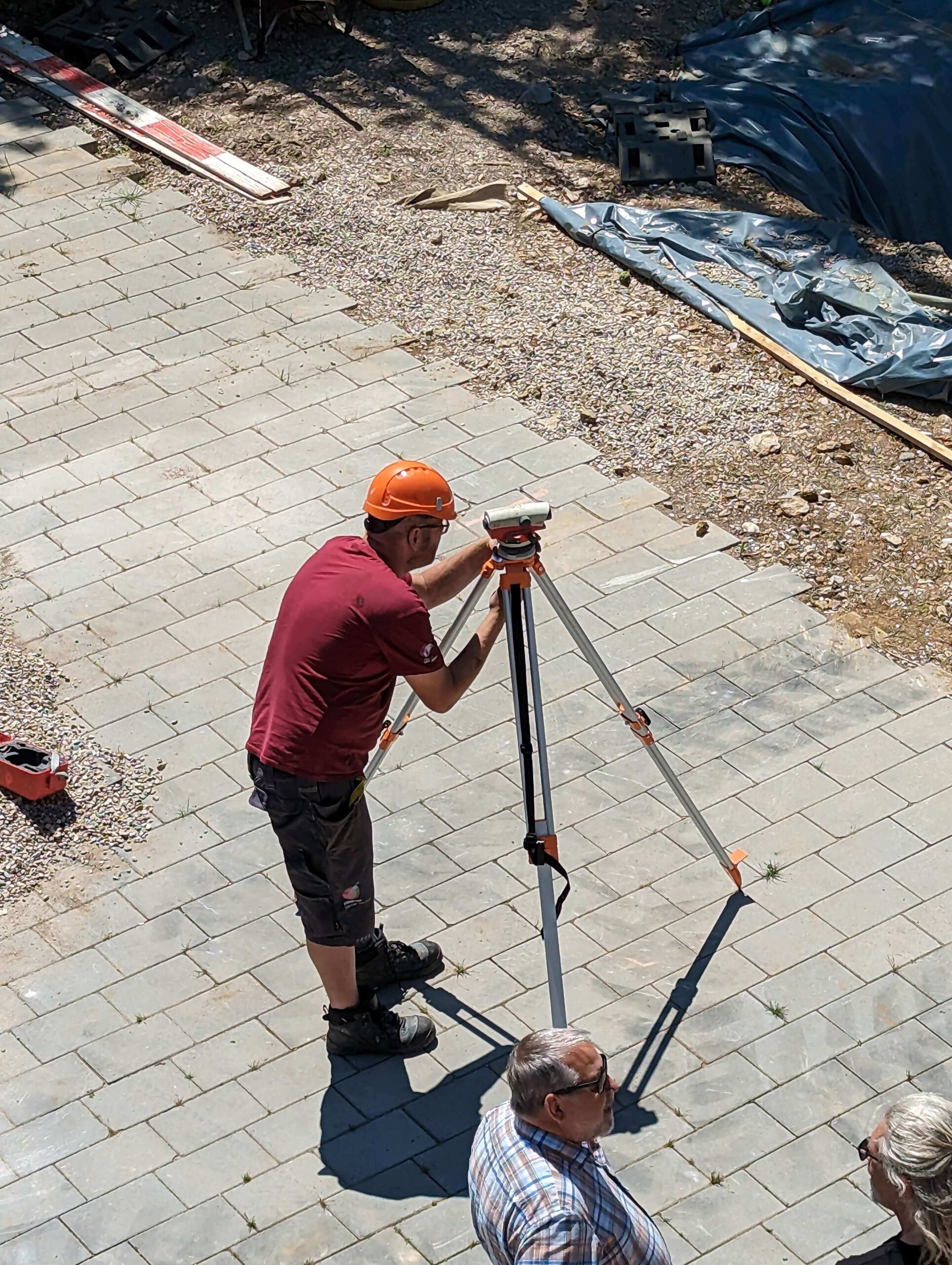 Vermessung einer neuen Pflasterfläche im Gartenbau Ein Vermessungstechniker prüft mit einem roten Tachymeter die neu angelegte Pflasterfläche im Garten.